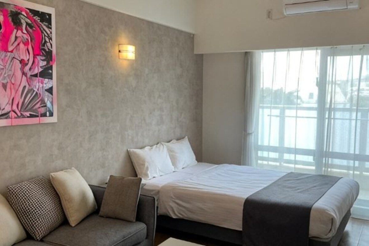 A modern hotel room with a bed, a sofa, a painting, and a large window.