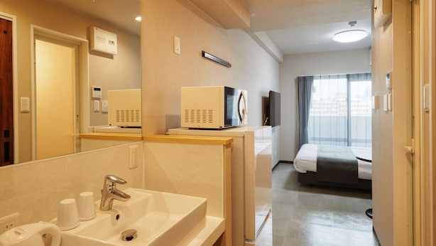 A hotel bathroom with a sink, mirror, and towel dispenser. - New Normal Hotel in MATSUYAMA (Naha)