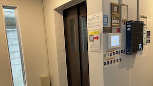 An elevator with a control panel, informational signs, and a door with a window. - New Normal Hotel in MATSUYAMA (Naha)