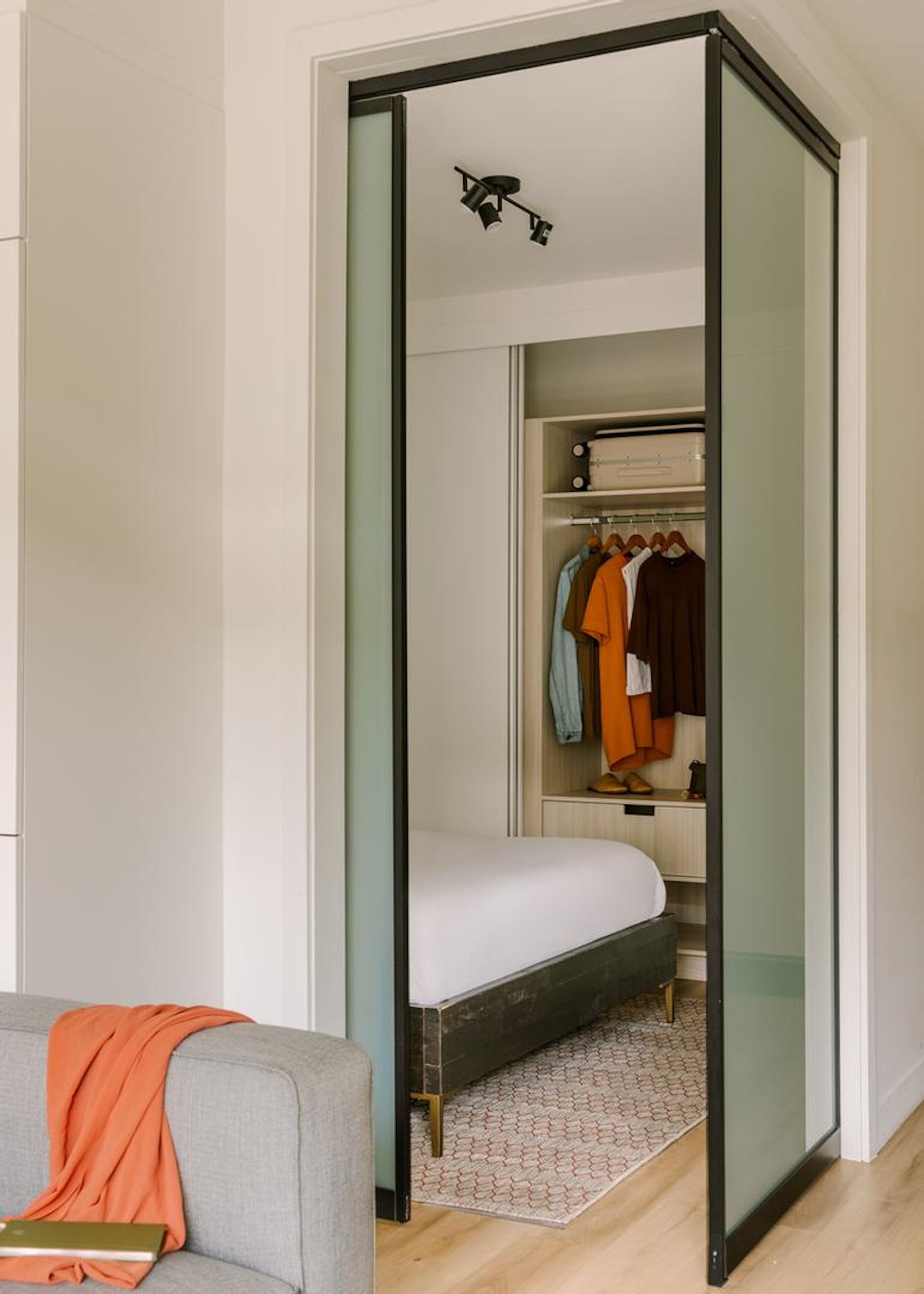 Una habitación con una cama, un sofá gris, un armario con puertas de cristal y una alfombra estampada.