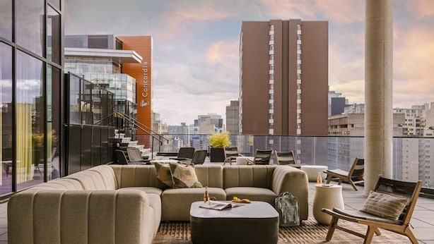 Un salon moderne avec un canapé d’angle, une table basse et un fauteuil, donnant sur un paysage urbain avec de hauts immeubles.