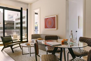 A modern living room with a glass table, leather chairs, a sofa, and a large window overlooking a building.