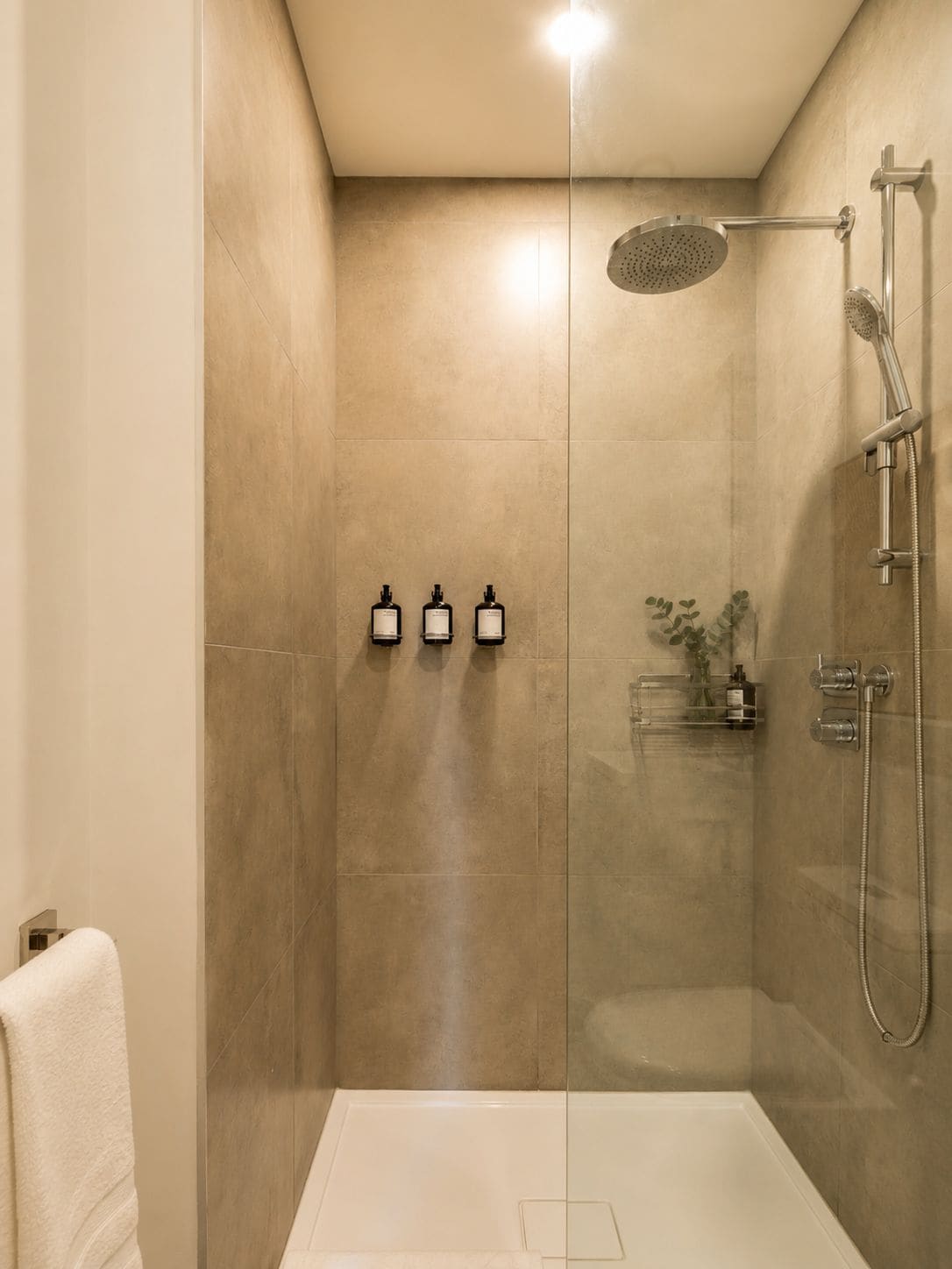 A modern shower with a handheld showerhead, a wall-mounted rain showerhead, and a handheld shower attachment.