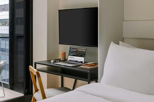 A hotel room with a bed, a desk with a laptop, a television, and a chair.