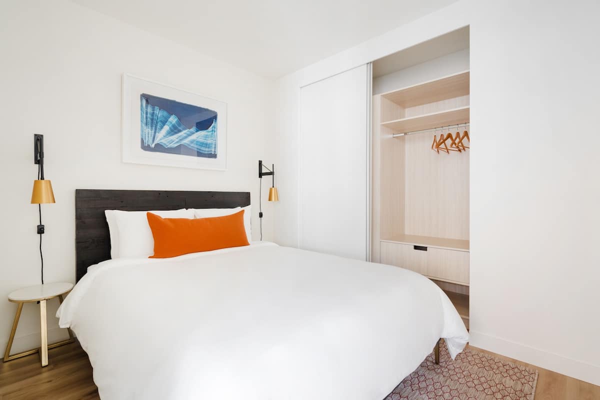 Habitación de hotel ordenada con una cama grande, una mesita de noche pequeña, un armario y una obra de arte enmarcada en la pared.