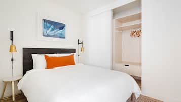 Une chambre d’hôtel bien rangée, avec un grand lit, une petite table de chevet, une armoire et une œuvre d’art encadrée au mur.