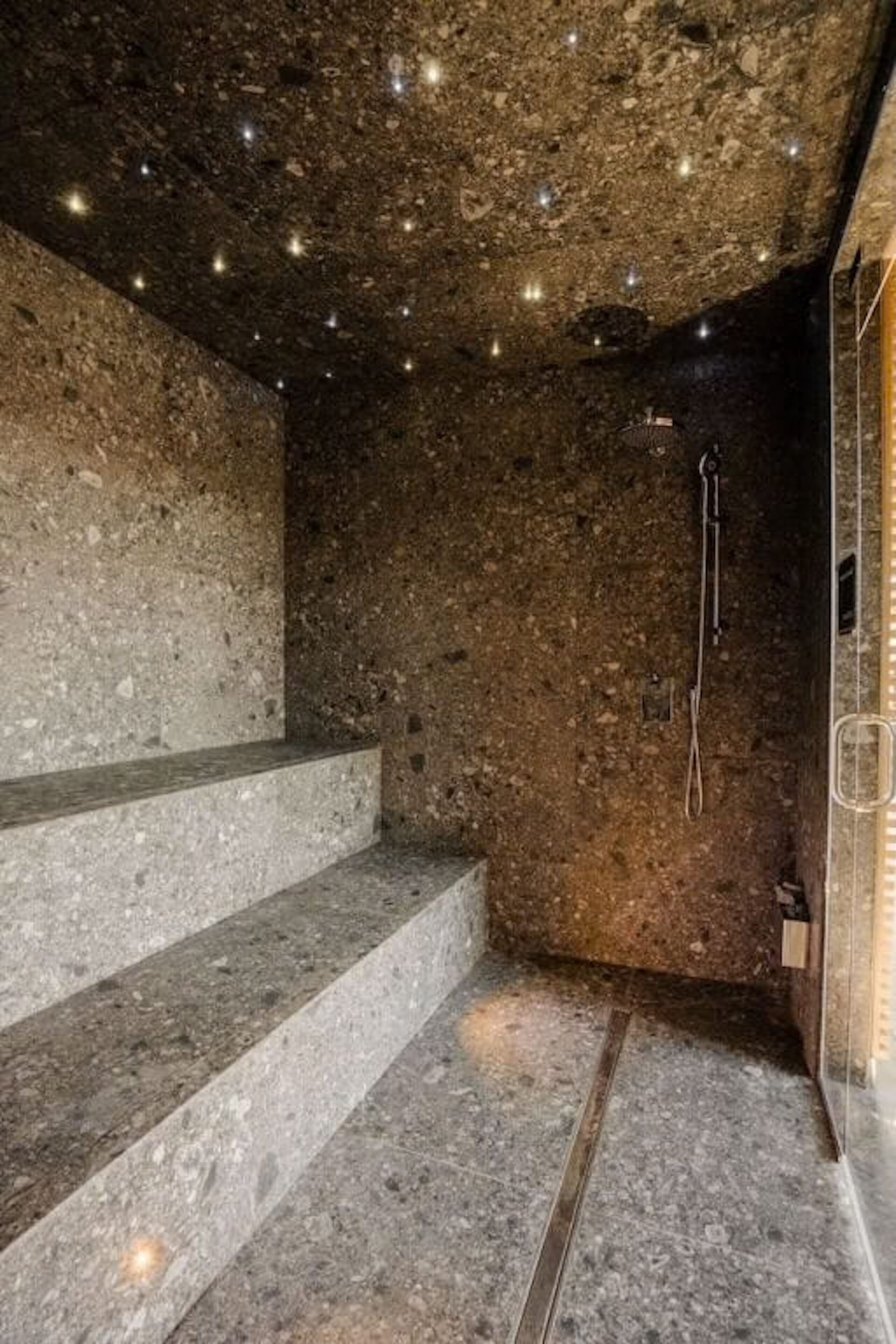 Una habitación con paredes de piedra, ducha, escalera y puerta de cristal.