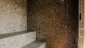 Una habitación con paredes de piedra, ducha, escalera y puerta de cristal.