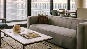 Un salon moderne avec un canapé, une table basse et une vue sur le paysage urbain, visible à travers de grandes fenêtres.