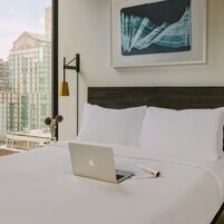 A hotel room with a bed, a laptop, a pen, and a framed artwork on the wall.