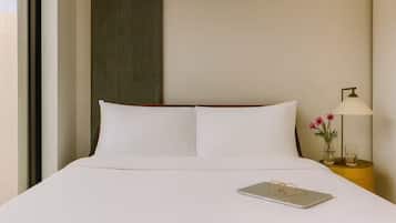 Una habitación de hotel con una cama, una mesita de noche con una lámpara, y un ordenador portátil sobre la cama.