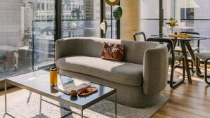 Un salon moderne comprenant un canapé, une table basse et un coin repas, avec de grandes fenêtres offrant une vue sur la ville.