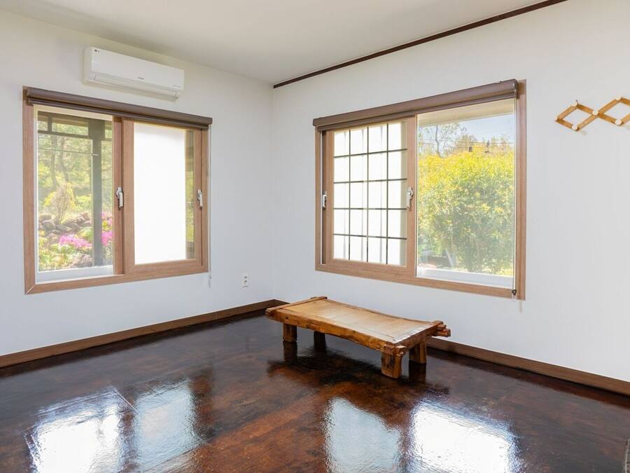 A room with two large windows, a wooden bench, and a wall-mounted air conditioner.