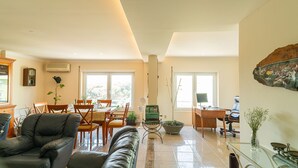A spacious living room with a leather sofa, dining area with wooden chairs, a green armchair, and a large window. - Family Comfort House (Cavaquinhas)