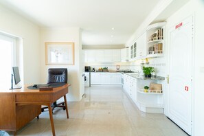 Une cuisine moderne avec des meubles blancs, un coin repas doté d’une table en bois et de chaises noires, et un tableau encadré accroché au mur.