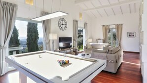 A spacious room with a pool table, a sofa, a TV, and a view of trees and a distant landscape. - Wonderful private villa for 12 guests with private pool, WIFI, A/C (Montecatini Alto)