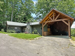 Une cabane rustique avec une cheminée en pierre, une véranda et un garage.