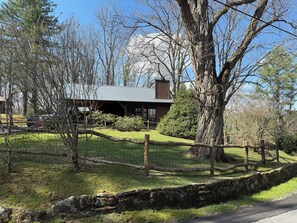 A rustic cabin with a metal roof, surrounded by a stone wall and a wooden fence.