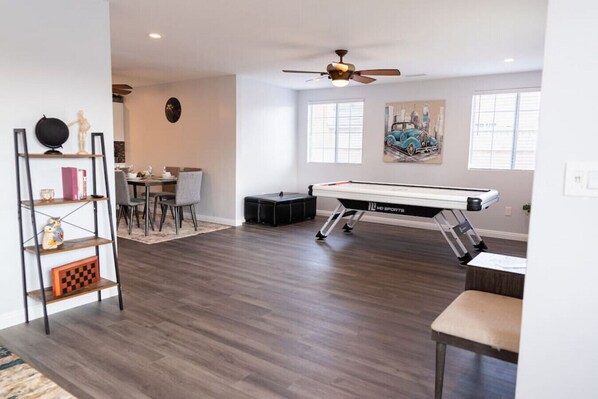 A spacious room with a pool table, a ping pong table, and a dining area with chairs and a table.