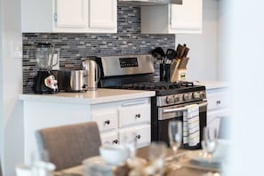 A modern kitchen with a gas stove, a kettle, a blender, and a toaster. There are white cabinets and a tiled backsplash.
