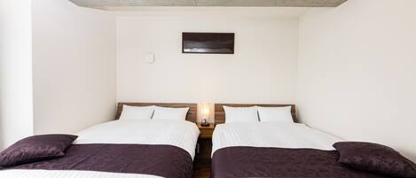 A room with two beds, a nightstand with a lamp, a small picture on the wall, and a concrete ceiling.