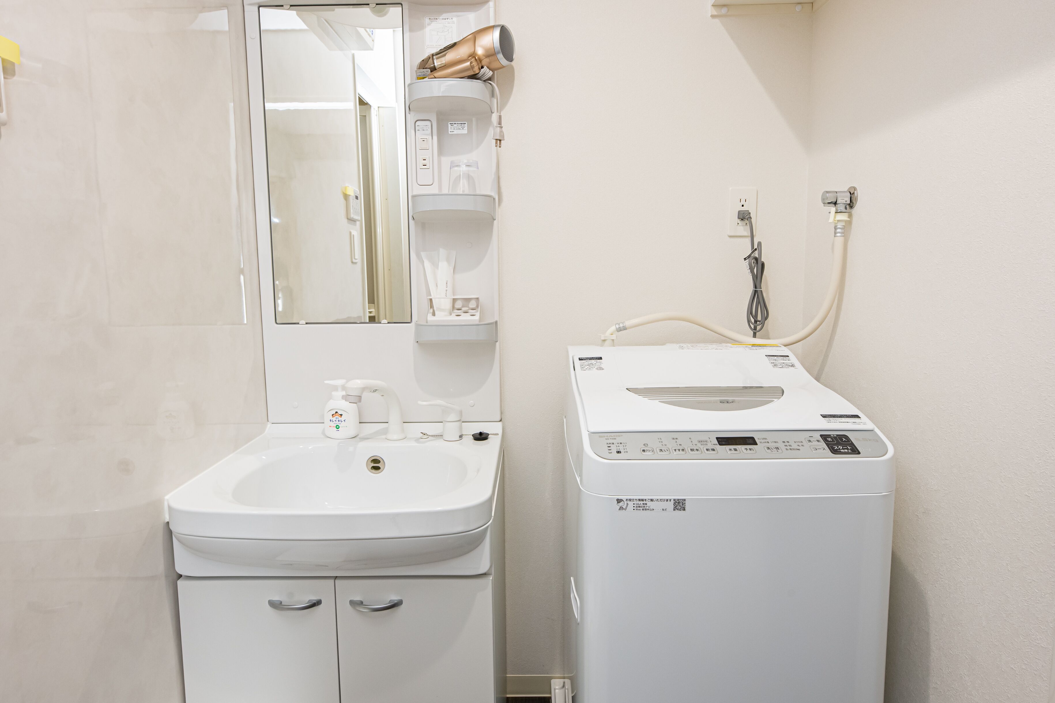 A bathroom with a sink, mirror, hairdryer, and a washing machine.