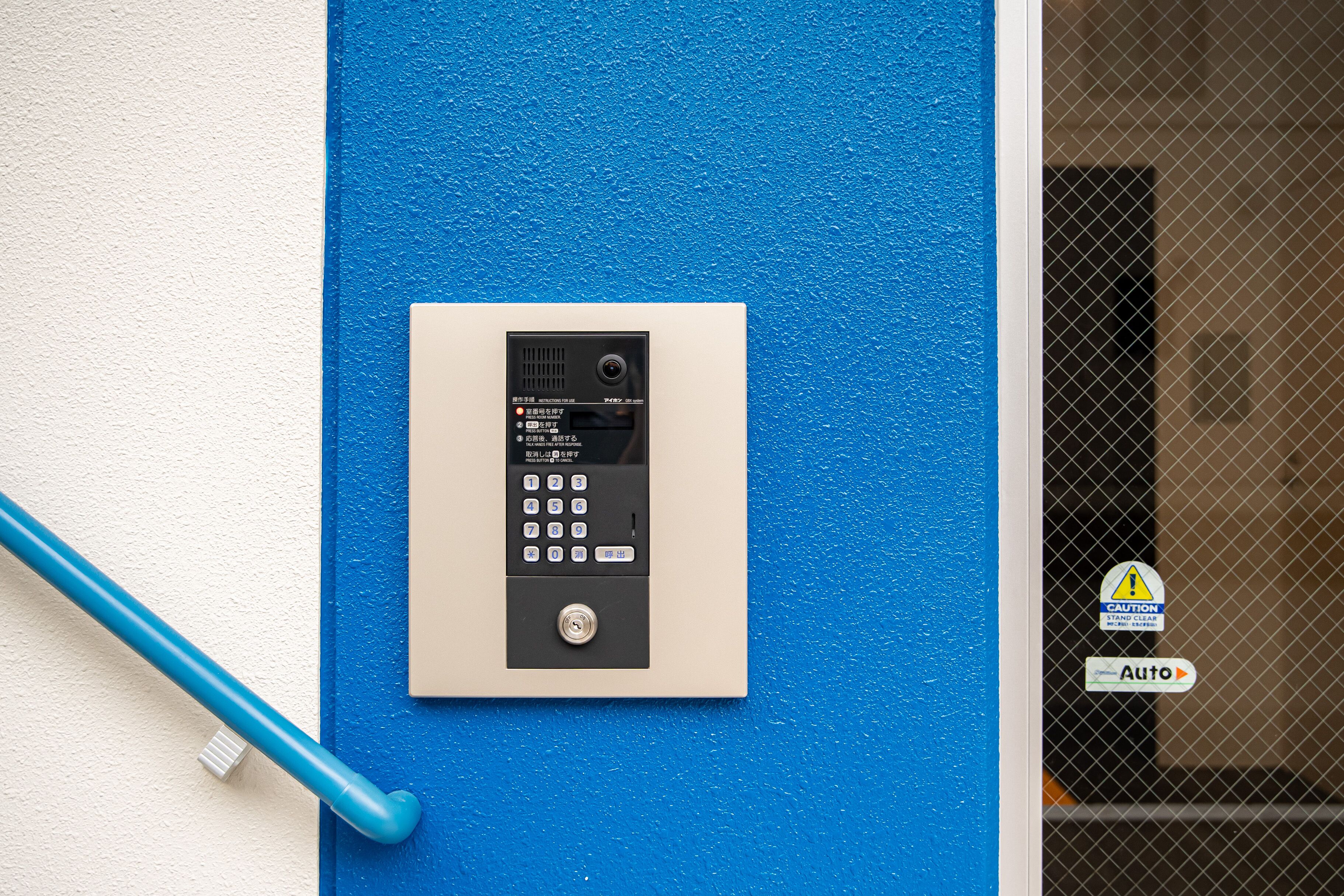 Un panel de teclado de seguridad en una pared azul, con una barandilla azul cerca.