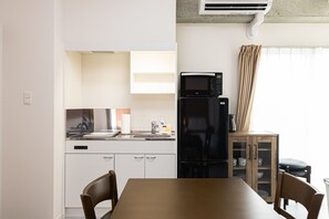 A compact kitchen with a refrigerator, microwave, and sink. There is a dining table with chairs and a cabinet with glass doors.