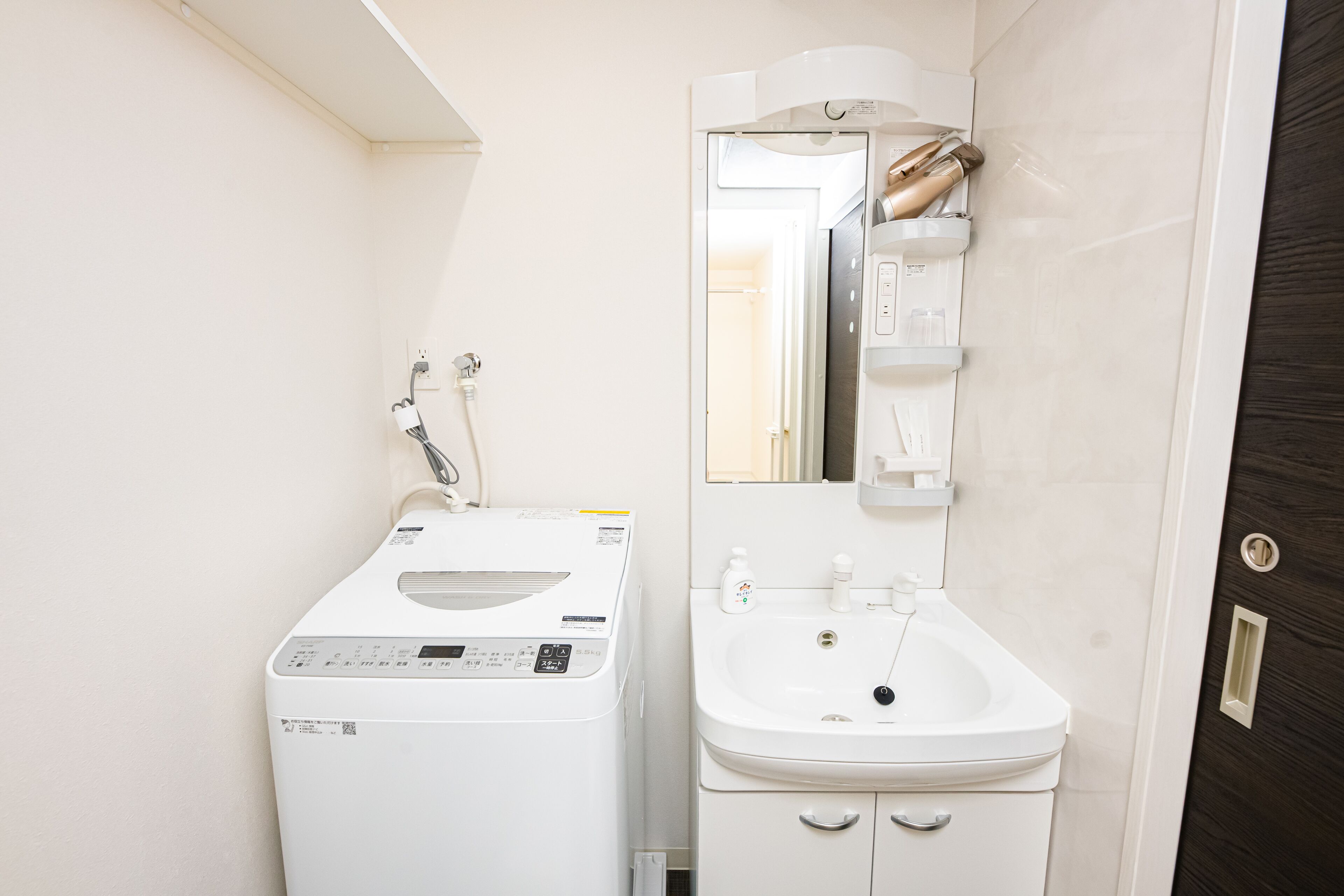 A compact bathroom with a washing machine, a sink, and a mirror.