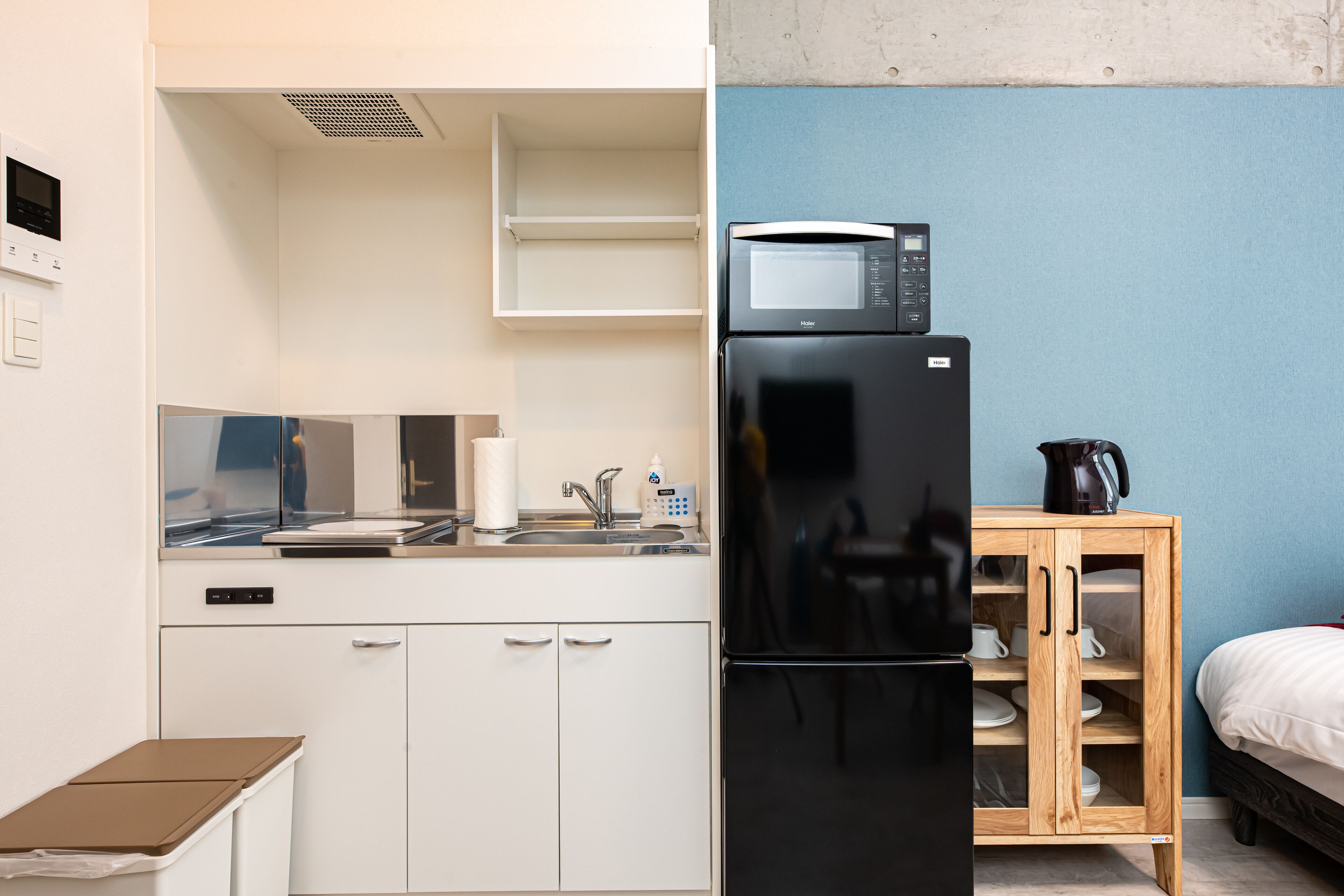 A compact kitchen with a refrigerator, microwave, and a wooden cabinet with shelves.