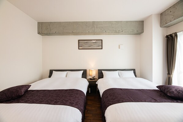 A hotel room with two beds, a nightstand with a lamp, a framed picture on the wall, and a window with curtains.