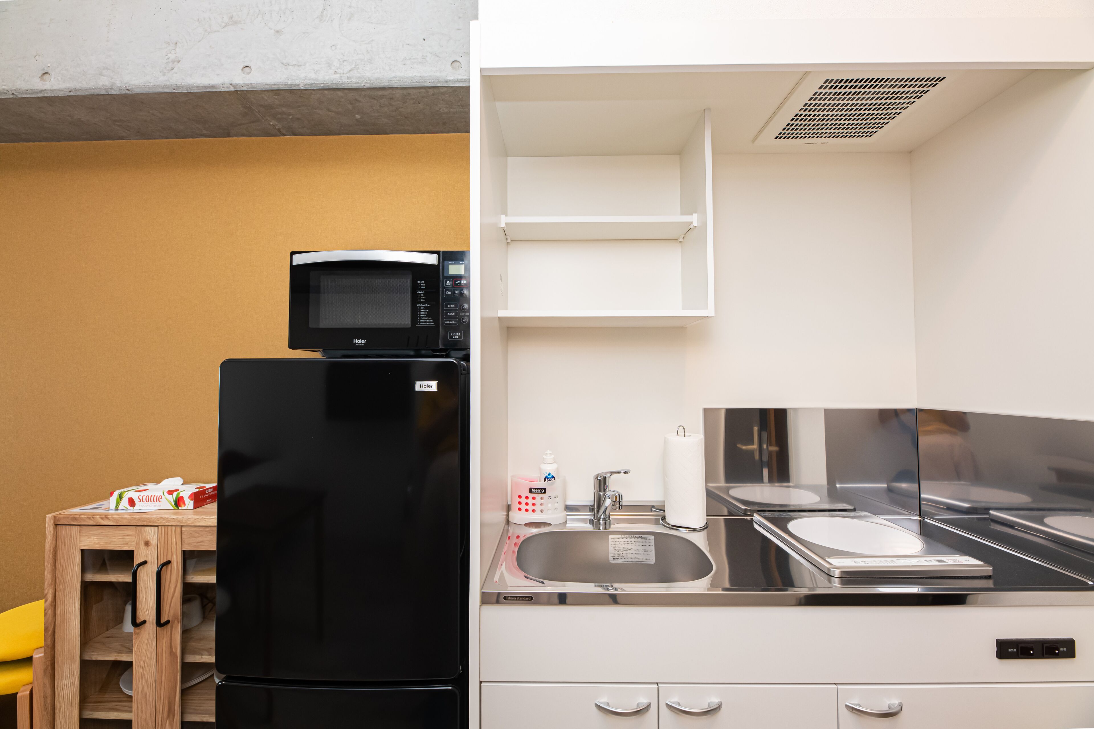 A compact kitchen with a black refrigerator, a microwave, a sink, and a small wooden table with a box on it.