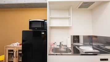 A compact kitchen with a black refrigerator, a microwave, a sink, and a small wooden table with a box on it.