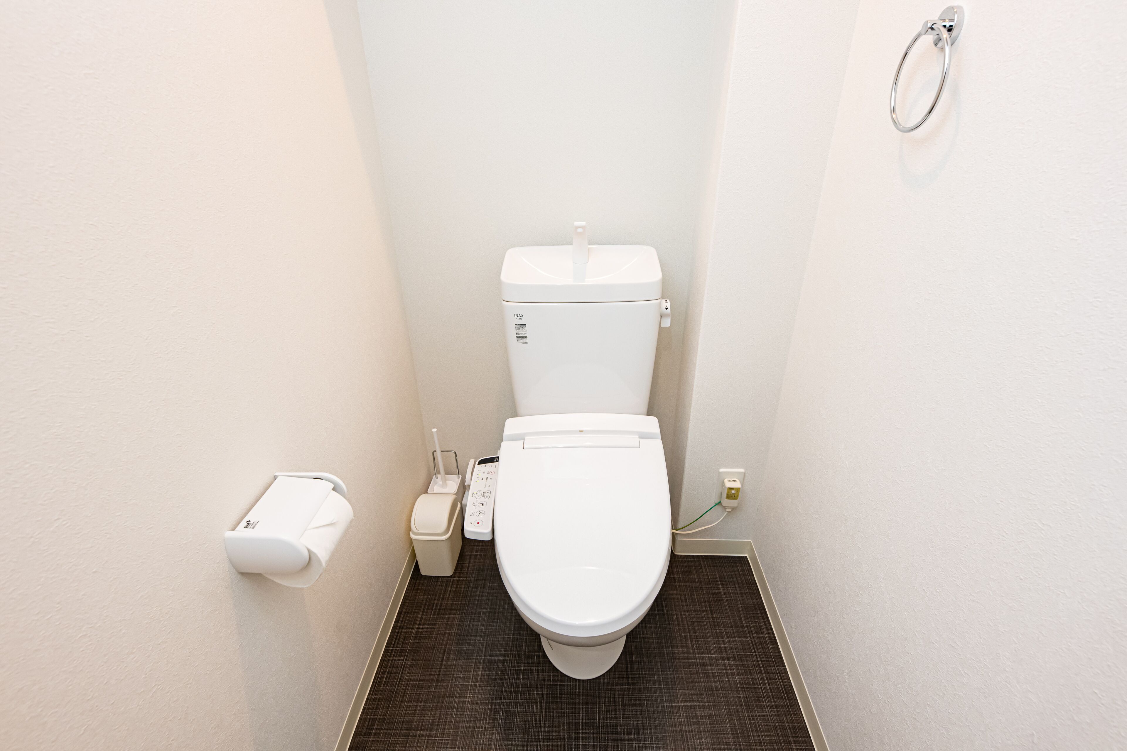 Ein kleines, modernes Badezimmer mit einer weißen Toilette, einem Toilettenpapierhalter und einem Handtrockner.