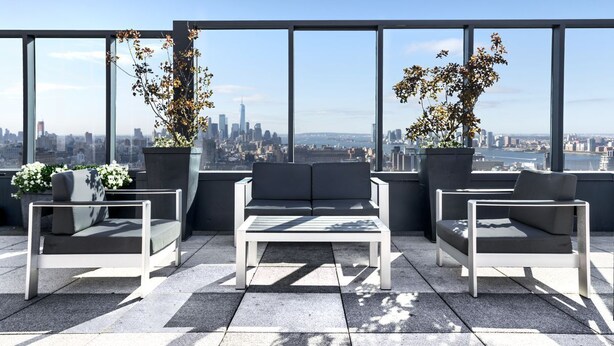 Terraço no terraço com vista para a cidade, com um sofá e duas poltronas, além de duas plantas em vasos.