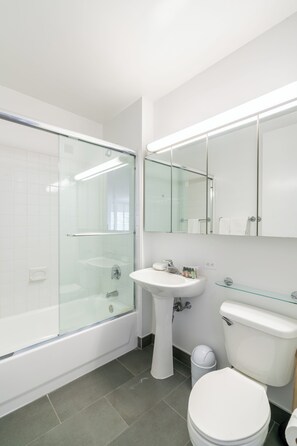 A modern bathroom with a glass-enclosed shower, a pedestal sink, a toilet, and a mirror above the sink.