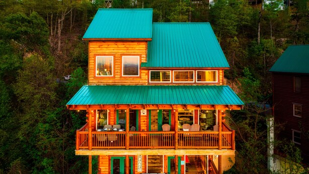 A two-story log cabin with a green roof, multiple balconies, and a porch area with outdoor seating. - Family-Friendly• Stunning Views • 7 Mi to Dollywood •Hot Tub• Highly Rated! (Sevierville)
