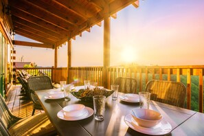 Area pranzo all'aperto con pergola in legno, sedie in vimini e tavolo imbandito per quattro, con piatti, ciotole e bicchieri.