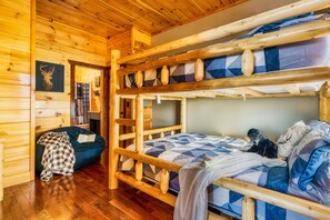 Una baita con un letto a castello, una coperta a quadretti su un sacco di fagioli e un quadro raffigurante un cervo appeso al muro.