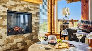 A cozy room with a stone fireplace, a wooden table with wine glasses and snacks, and a view of the outdoors. - Family-Friendly• Stunning Views • 7 Mi to Dollywood •Hot Tub• Highly Rated! (Sevierville)