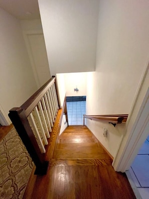A wooden staircase with a handrail, leading to a room with a tiled floor and a small table. - Ocean tranquility 2 br house  free parking prime location downtown Myrtle Beach (Myrtle Beach)