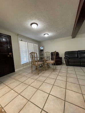 A living room with a dining table and chairs, a black leather sofa, and a television on a stand. - Ocean tranquility 2 br house  free parking prime location downtown Myrtle Beach (Myrtle Beach)
