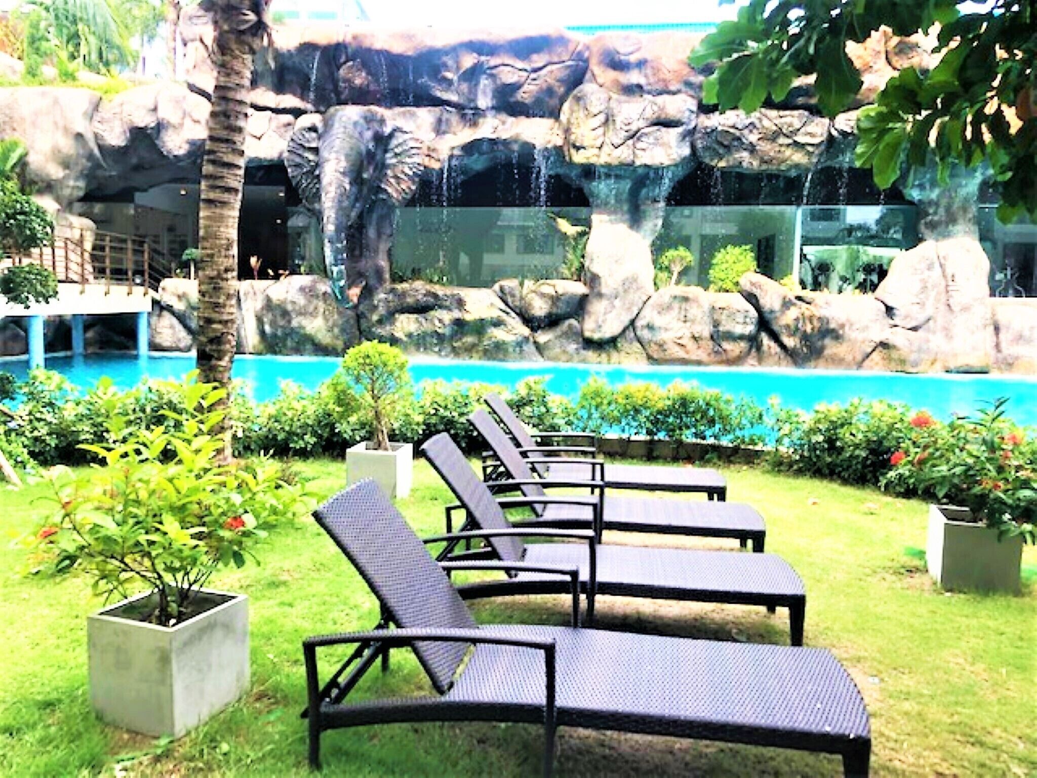 A pool area with lounge chairs, a waterfall, and a rocky backdrop.