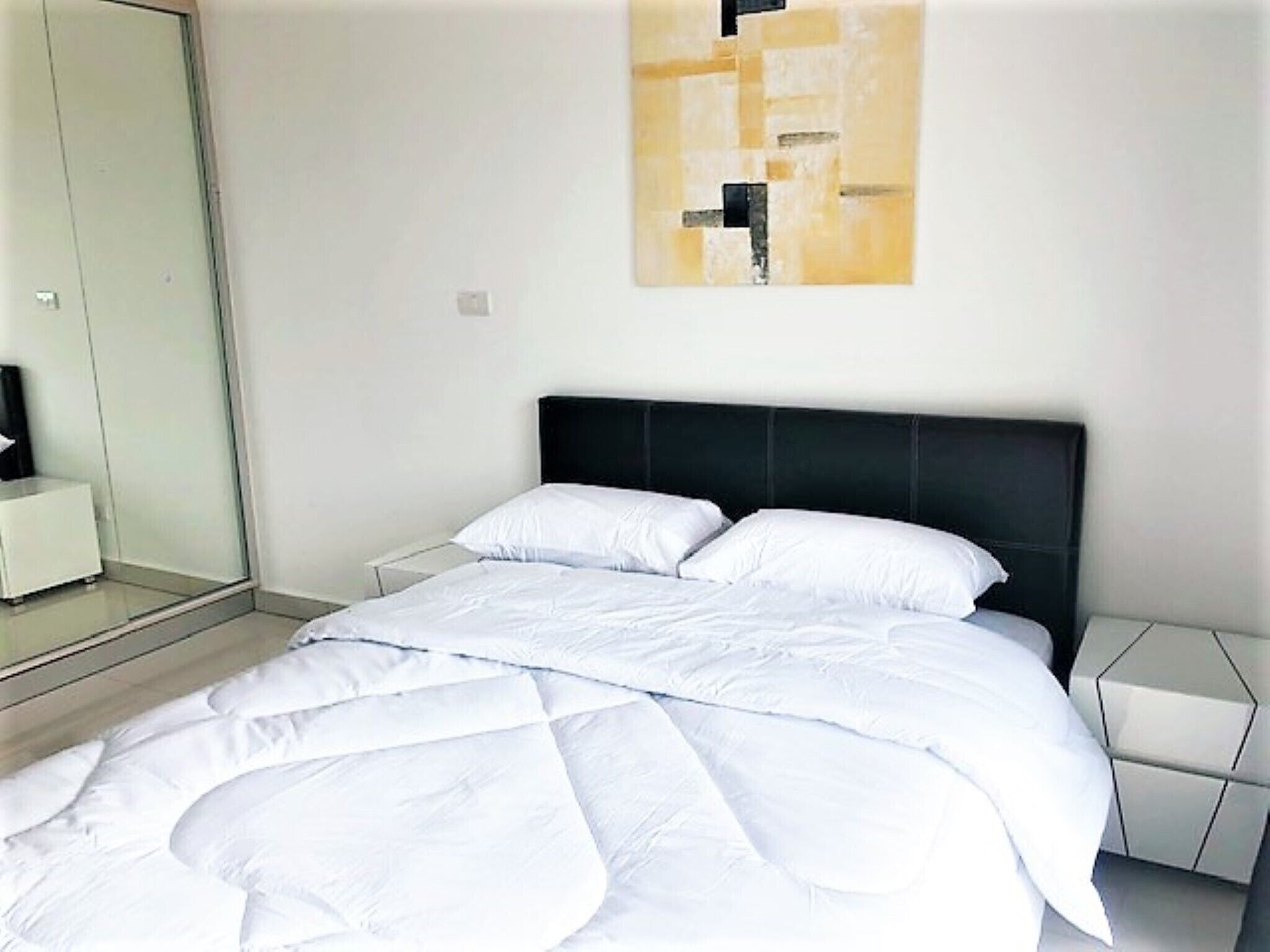 A modern bedroom with a large bed, a black headboard, and a minimalist wall art piece.