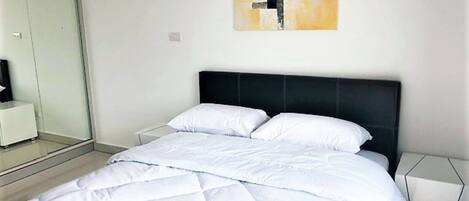 A modern bedroom with a large bed, a black headboard, and a minimalist wall art piece.