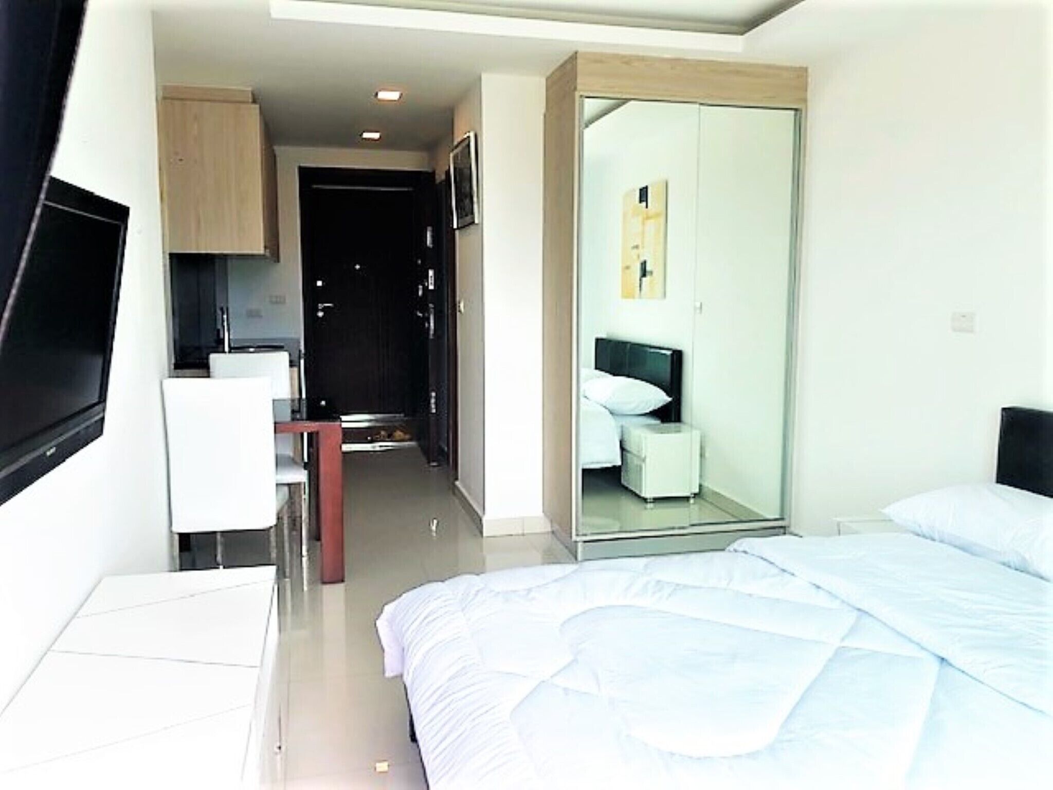 A modern hotel room with a bed, a small bedside table, a mirror, and a wardrobe.