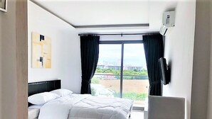 A hotel room with a bed, a desk, a chair, a TV, and a large window with curtains. - Laguna Beach 3 The Maldives - top Floor Studio (Pattaya)