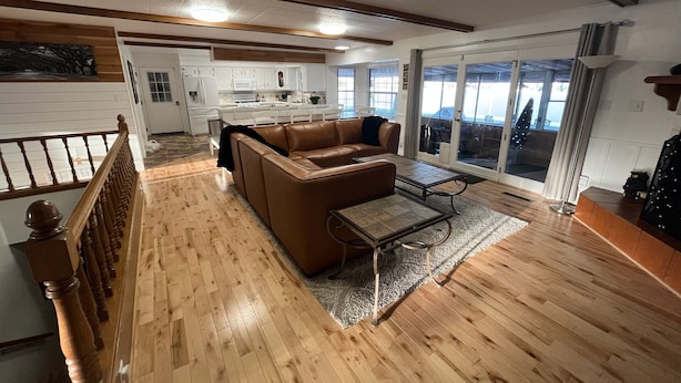 A spacious living area with a brown leather sofa, a coffee table, and a wooden floor. There is a kitchen in the background with white cabinets and a dining area with a table and chairs. - Indoor Pool , Hot Tub, Game Room & Gym  (South Jordan)