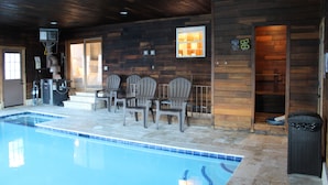 An indoor swimming pool with a wooden deck, chairs, and a trash bin. - Indoor Pool , Hot Tub, Game Room & Gym  (South Jordan)