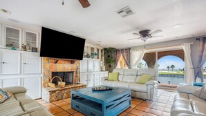 A living room with a stone fireplace, white cabinets, a blue coffee table, and a large TV. - Backyard fishing & birdwatching - 3,600sqft home near beach w/ hot tub, gazebo (Corpus Christi)
